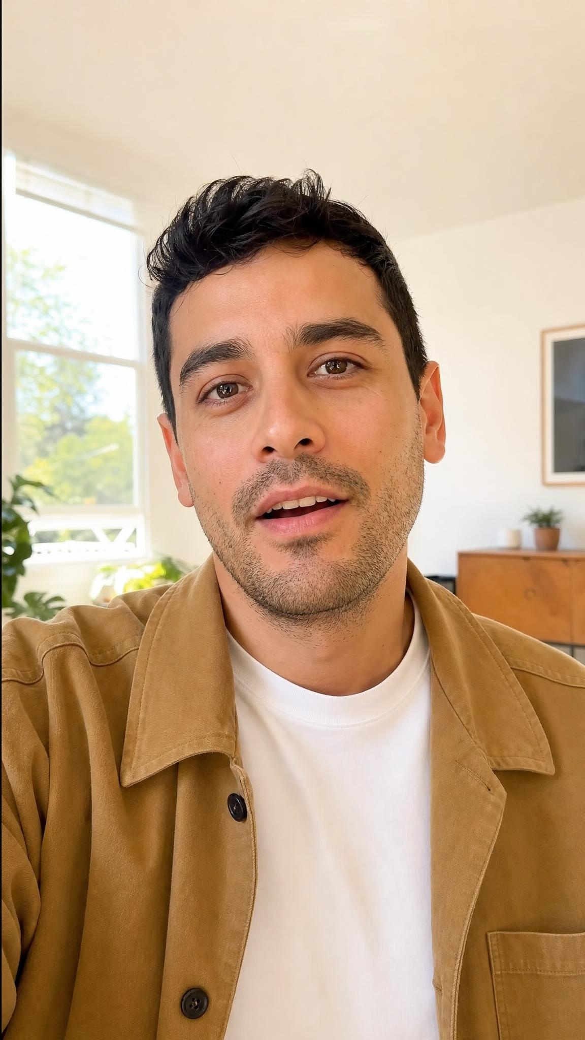Clothing creator in an oversized camel chore jacket, bright apartment portrait